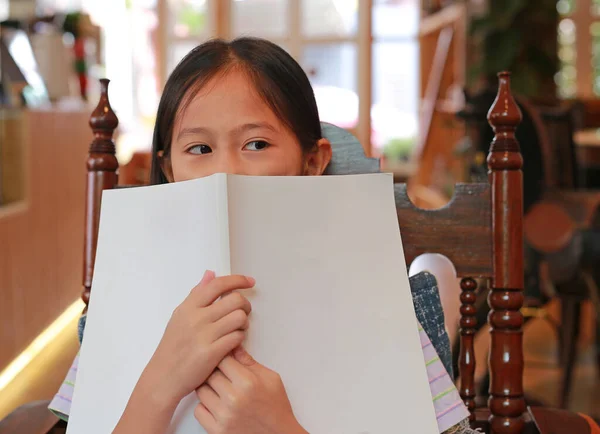 アジアの女の子子供カバー顔とともに白い本と横に見ながら読書で図書館 — ストック写真