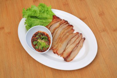 Kızarmış domuz eti, ahşap zemin üzerinde beyaz tabakta baharatlı ekşi soslu domuz budu..