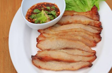 Kızarmış domuz eti, ahşap zemin üzerinde beyaz tabakta baharatlı ekşi soslu domuz budu..