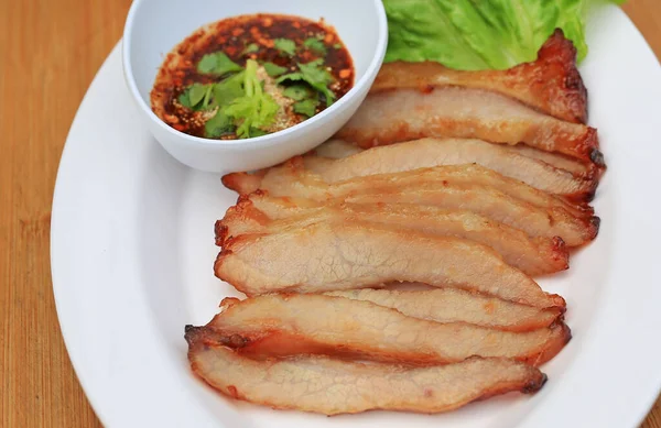 Kızarmış domuz eti, ahşap zemin üzerinde beyaz tabakta baharatlı ekşi soslu domuz budu..