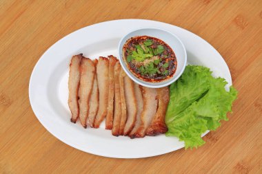 Kızarmış domuz eti, ahşap zemin üzerinde beyaz tabakta baharatlı ekşi soslu domuz budu..