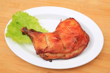 Kızarmış tavuk budu beyaz tabakta ahşap arka planda.