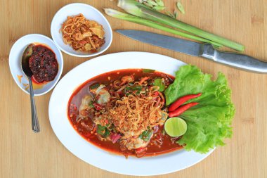 Baharatlı salatada istiridye, beyaz tabakta acı biber ve ahşap arka planda kızarmış soğan ile servis ediliyor..