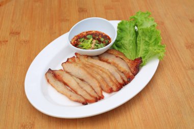 Kızarmış domuz eti, ahşap zemin üzerinde beyaz tabakta baharatlı ekşi soslu domuz budu..