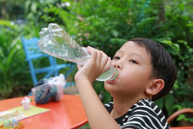 Susamış Asyalı çocuk bahçedeki plastik şişeden su içiyor..