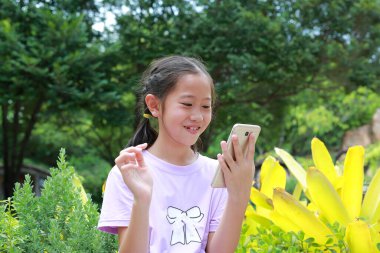 Parkta akıllı telefon kullanan heyecanlı Asyalı kız çocuğu. Uzak iletişim konsepti.