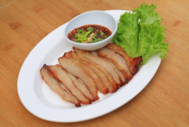 Kızarmış domuz eti, ahşap zemin üzerinde beyaz tabakta baharatlı ekşi soslu domuz budu..