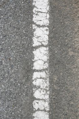 Asfalt yolda beyaz çizgiler çatlamış. Eski beyaz yol hattı, yakın plan..