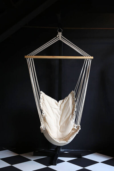 White fabric cradle hang indoor at dark living room. Hammock hanging swing against black wall.