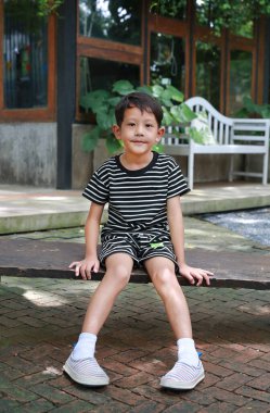 Bahçedeki ahşap bankta oturan Asyalı küçük çocuk portresi.