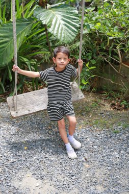 Asyalı küçük çocuk bahçede salıncakta sallanıyor..