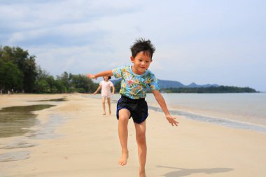 Happy Asian little boy child and girl kid having fun running on tropical sand beach at sunrise. Happy family sister and brother enjoy in summer holiday.