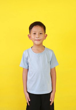 6 yaşında gülümseyen Asyalı bir çocuğun portresi sarı arka planda izole edilmiş kameraya bakıyor..