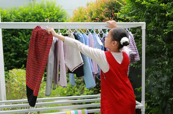 アジアの少女は家の近くの庭で衣服の柵に洗濯物を掛ける ロイヤリティフリーのストック画像