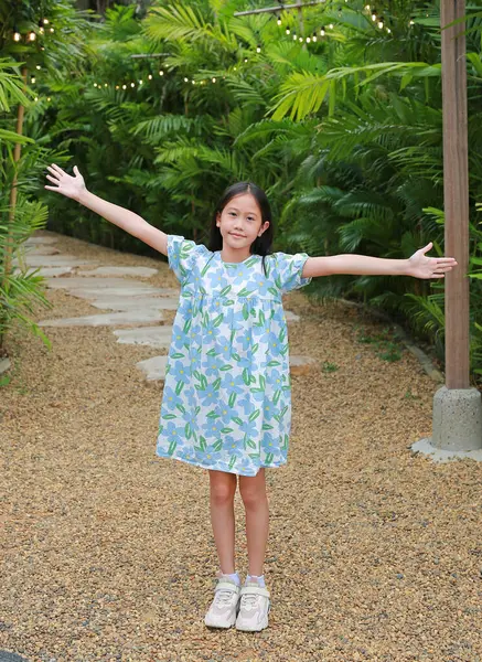 かわいいアジアの少女は庭に立っている間 腕を伸ばしたり 腕を保ちます ロイヤリティフリーのストック画像