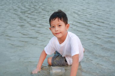 Asyalı çocuğun portresi kumsalda yatarken kum oynamaktan zevk alıyor..