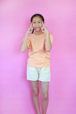 Gülümseyen Asyalı genç kız yeni bir fikir jesti düşünüyor işaret parmağı ile beyin pembe stüdyo arka planında izole.