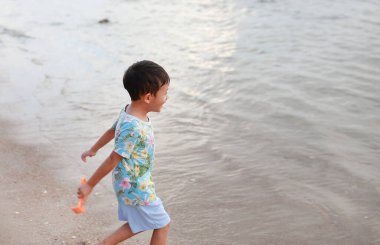 Kum ve denizde oynarken mutlu bir Asyalı çocuğun portresi..