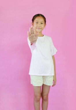 Yumuşak odaklı Asyalı kız çocuğu, pembe stüdyo arka planında izole edilmiş dur işareti gösteriyor. Avuç içine odaklan.