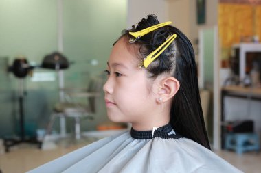 Asyalı bir kızın bir güzellik salonunda saçını kestirirken portresi. Kapat..