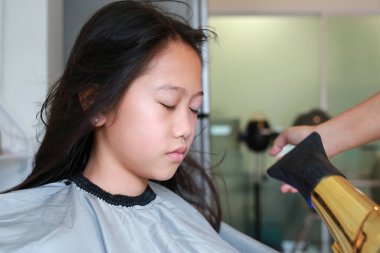 Saçını fırça ve saç kurutma makinesiyle düzleştiren Asyalı bir kız. Kuaför çocuk saçını kurutuyor..