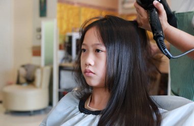 Kuaförde Asyalı ergen kızın saçını kurutup tarayan profesyonel stilistin portresi. Yakın çekim..