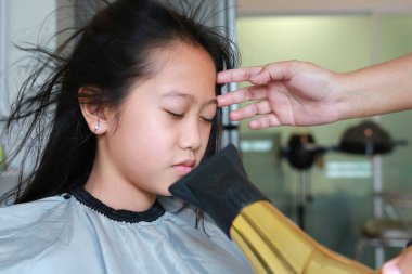 Saçını fırça ve saç kurutma makinesiyle düzleştiren Asyalı bir kız. Kuaför çocuk saçını kurutuyor..