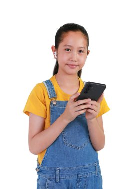 Beyaz arka planda izole edilmiş müzikle eğlenmek için akıllı telefon ve kablosuz kulaklık kullanan Asyalı kız çocuğu.