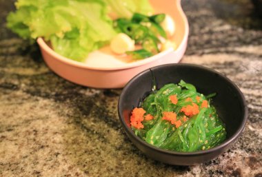 Taze yeşil wakame deniz yosunu salatası üzerine karides yumurtası ve masada küçük bir kase..