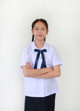 Okul üniformalı güzel Asyalı kız öğrencinin portresi beyaz stüdyo geçmişine karşı kollarını kavuşturmuş duruyor..