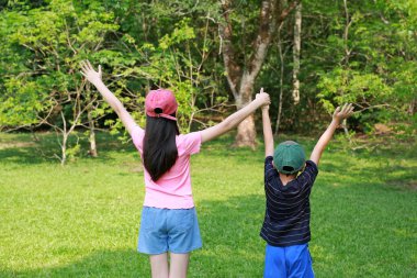 Asyalı kız ve çocuğun arka planda el ele tutuşmuş şapka takıp el sallamaları. Merhaba ya da güle güle..