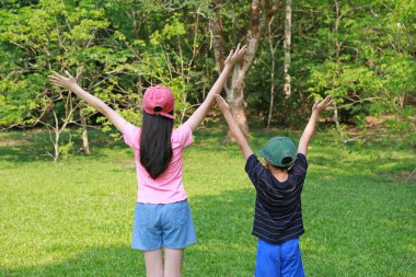 Bahçede dikilirken, şapkalı, avuç içi el sallayan Asyalı kız ve oğlan çocuğu..