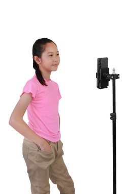 Beyaz stüdyo arka planında izole edilmiş üç ayaklı telefon kullanan Asyalı blogcu kız çocuğu. Sosyal medyada paylaşmak için mobil uygulama üzerinde içerik oluşturan çocuk.