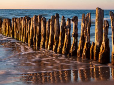 Baltık Denizi üzerinde gün batımı. Eski ahşap dalgakıranın manzarası ve sudaki yansıması. Mielno, Polonya. Batı Pomeranya. Doğu Avrupa