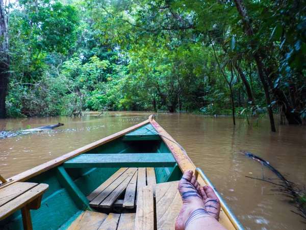 Legs with tattoos on a wooden boat and a view of the green wall of the Amazon rainforest, Amazon green hell. Selva on the border of Brazil and Peru. Amazonia. South America.
