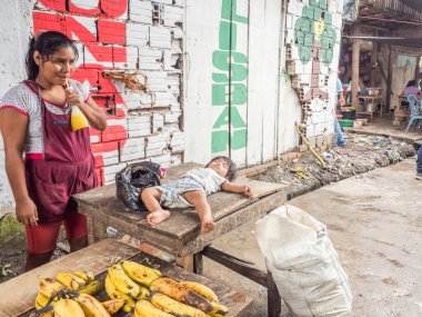 Belen, Iquitos, Peru - 27 Mart 2018: Iquitos 'taki Belem Market' te muz satan genç kadın ve çocuk ahşap masada uyuyor Beln.