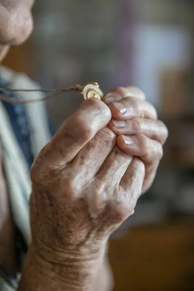 Hands of an old woman praying and holding a gold medal with Our Lady