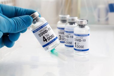 Elinde COVID-19 aşı tüpü var. Üzerinde 4 doz ve 1., 2., 3. aşılar var. Coronavirus aşı şişesini elinde tutan doktor etiketinde dördüncü doz aşının adı yazılı.