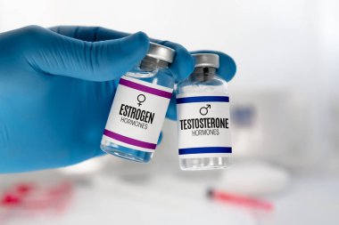 Testosteron ve östrojen hormonu tedavisi için iki enjeksiyon tüpü olan bir doktorun eli. Testosteron ve Östrojen hormonu dengesi terapisi için şişeleri olan doktor.