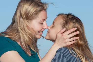 Genç, neşeli bir anne ve küçük kızı burunlarına dokunuyor ve dışarıda kaynaşıyorlar.