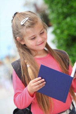 Sırt çantası ve defterleri açık havada olan neşeli ilkokul öğrencisinin portresi.