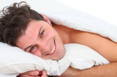 Beyaz arka planda yatakta gülümseyen bir genci kapat.