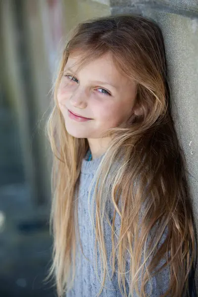 Duvara yaslanmış, gülümseyen kameraya bakan sevimli küçük kız. 