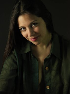 Düğmeleri iliklenmemiş yeşil gömlekli, uzun siyah saçlı, düşük ışıklı genç seksi bir kadın. 