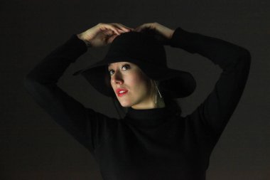  Koyu arkaplanda siyah şapka ve süveter giyen zarif esmer bir kadının portresi.