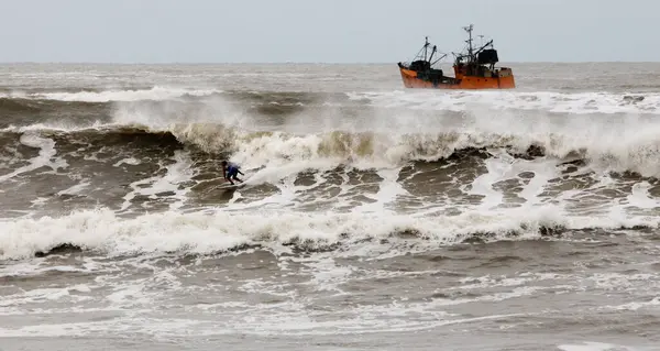 Bulutlu bir günde fırtınalı bir deniz ve uzakta bir balıkçı teknesi. 
