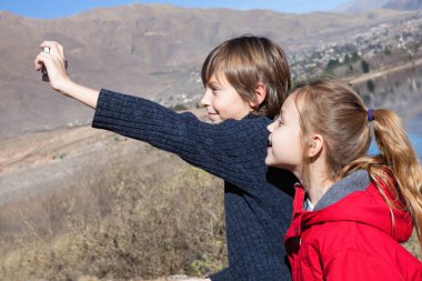 two cheerful kids, brother  and sister taking pictures of nature outdoors clipart