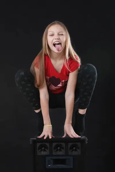 Havalı sarışın bir kızın portresi büyük bir hoparlör kutusuna oturmuş suratını buruşturuyor ve siyah arka planda dilini dışarı çıkarıyor.