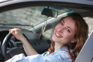 Sürücü koltuğunda gülümseyen ve kameraya bakan mutlu genç kadının yakın plan portresi.