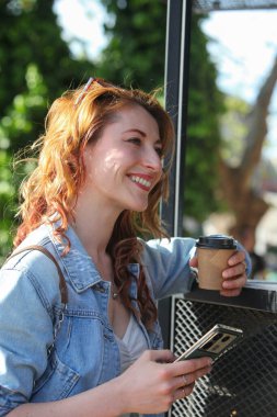 Caddedeki kaldırımdaki kafede kahve içip cep telefonu kullanan güzel bir kadının portresi.